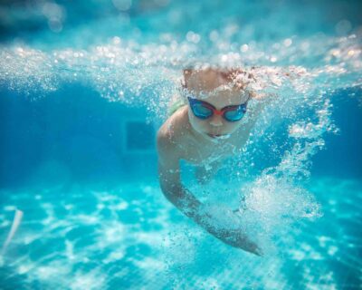 A young boy is swimming in a pool surrounded by clear blue water in Albuquerque, NM
