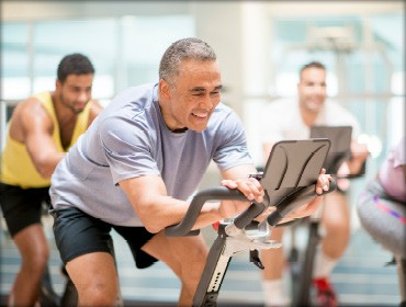 A man pedaling on an exercise bike inside a gym in Denver, CO