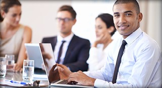 A man in a business suit sits at a table with colleagues engaged in discussion in Denver, CO