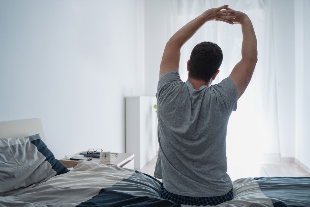 The Man stretches muscles on the bed in the bedroom in the morning